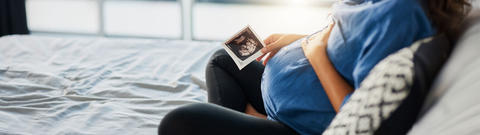 Schwangere Frau sitzt auf dem Bett und hält ein Ultraschallbild