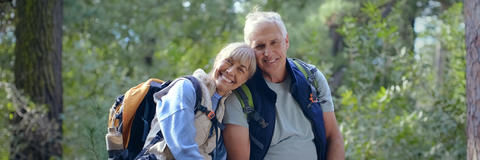 Mann und Frau in Wanderkleidung sitzen auf einem Baumstamm im Wald