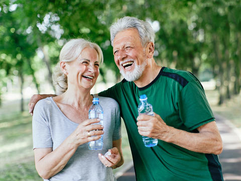 Frau und Mann halten Wasserflaschen in ihren Händen und lachen