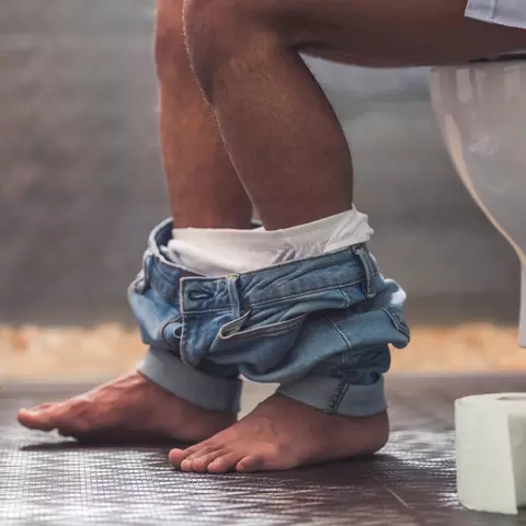 Person sitzt auf der Toilette neben ihre eine Rolle Klopapier
